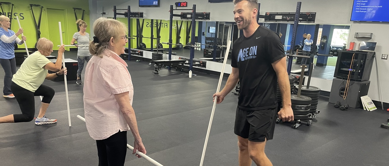 Jake Raecker explains PVC pipe exercise to a client at Age On Fitness
